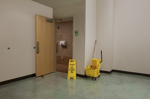 cuarto de baño de empresa con cubo de fregona y cartel de precaucion